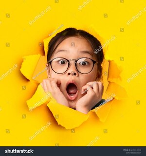 Stock photo shocked asian girl looking through hole in torn orange paper expressing exciement 